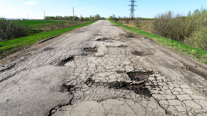 The texture of cracked old asphalt in need of repair. The road is full of holes and potholes. Pit...