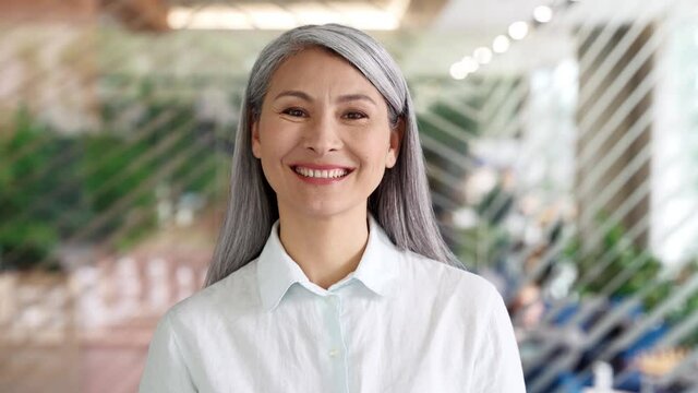 Happy confident smiling middle aged adult Asian older senior female businesswoman corporation ceo in modern office looking at camera. Business woman executive concept. Closeup portrait headshot.