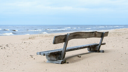 Fototapeta na wymiar Sea view and wooden bench in the sand dunes on a windy day.