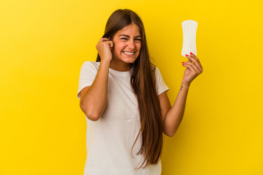 Young caucasian woman holding a compress isolated on yellow background covering ears with hands.