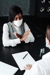African American woman in a medical mask shows with her hands the refusal of the doctor from voluntary vaccination