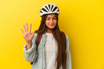 Young student caucasian woman wearing a bike helmet isolated on yellow background smiling cheerful showing number five with fingers.