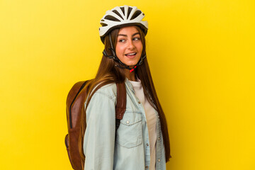 Young student caucasian woman wearing a bike helmet isolated on yellow background looks aside smiling, cheerful and pleasant.