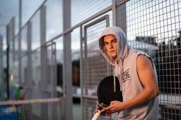 Young man with urban style takes a break with the phone trains after playing paddle tennis on an outdoor court