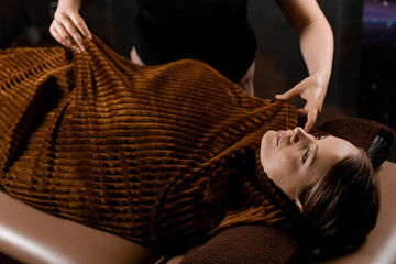 Full body wrap in warm blanket after chocolate massage beauty treatment for female model in spa.