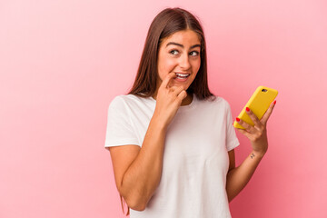 Young caucasian woman holding a mobile phone isolated on pink background relaxed thinking about something looking at a copy space.