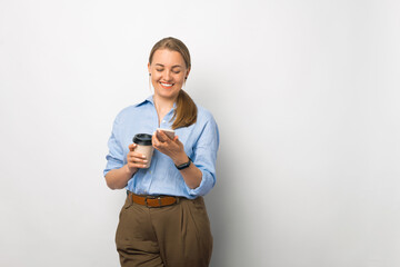 Photo of beautiful young business woman using smartphone and holding paper cup of coffee to go over white background - obrazy, fototapety, plakaty
