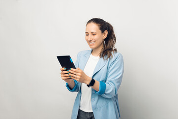 Photo of young beautiful woman in blue jacket using tablet over white wall