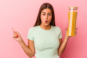 Young caucasian woman holding a pasta jar isolated on pink background pointing to the side