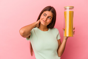 Young caucasian woman holding a pasta jar isolated on pink background touching back of head, thinking and making a choice.