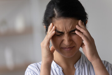 Unwell millennial Indian female touch head suffer from migraine or headache. Unhealthy young mixed race woman struggle with dizziness or blurry vision, have eyesight problems. Healthcare concept.
