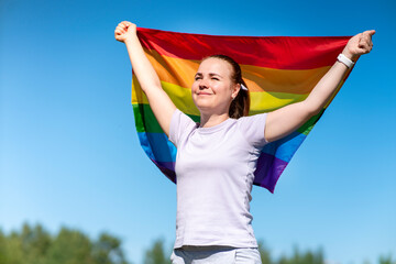 Portrait of young lesbian happy proud woman, beautiful girl is waving rainbow LGBT color gay flag...