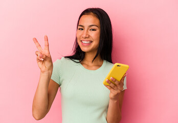 Young Venezuelan woman holding a mobile phone isolated on pink background showing number two with fingers.