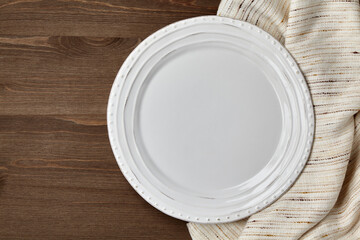 White ceramic plate and crumpled linen tablecloth on a dark wooden table