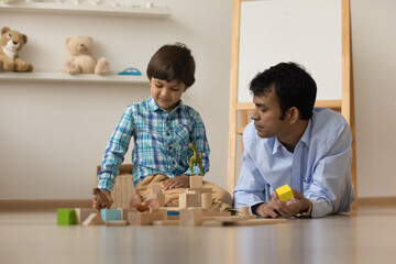 Fototapeta premium Loving young Indian father have fun play with block bricks with small ethnic son at home. Caring mixed race dad engaged in playful game activity with biracial boy child. Family weekend concept.