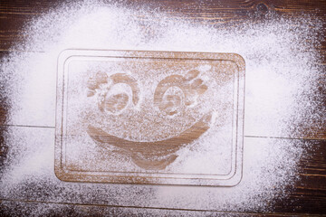 Funny face is painted on flour. Funny drawn man. Wooden surface is sprinkled with white powder, imitation of snow. Mock up.
