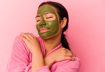 Young venezuelan woman wearing a bathrobe and facial mask isolated on pink background