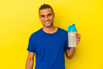 Young venezuelan man drinking a protein shake isolated on yellow background happy, smiling and cheerful.