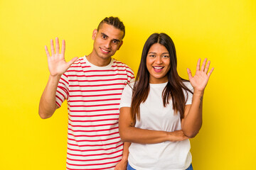 Young latin couple isolated on yellow background smiling cheerful showing number five with fingers.