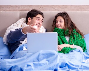 Sick wife and husband in bed with laptop