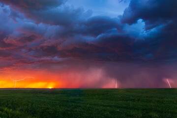 Obraz na płótnie Canvas Lightning bolts strike at sunset along the Wyoming / Colorado border at sunset. The last remnants of the sun can be seen setting along the horizon with color hues of pinks, purples, reds, and oranges.