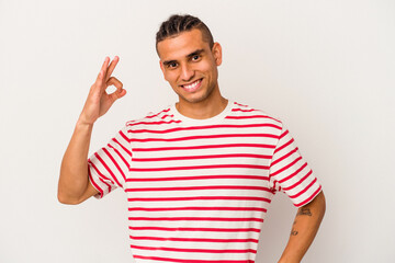 Naklejka premium Young venezuelan man isolated on white background winks an eye and holds an okay gesture with hand.