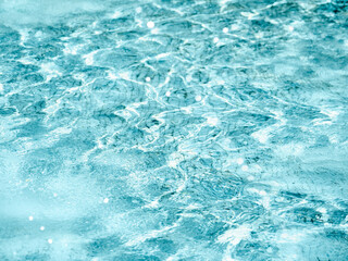 Sun beams on surface of water in swimming pool or fountain with blue mosaic bottom. Abstract background with wavy pattern of clear transparent water.