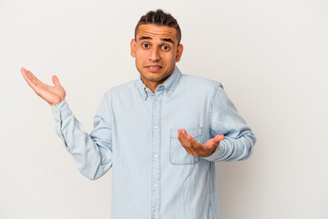 Young venezuelan man isolated on white background confused and doubtful shrugging shoulders to hold...