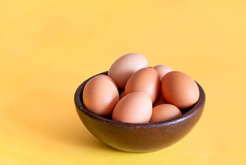 Eggs on a artesanal brown bowl on a yellow background