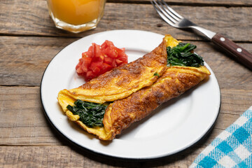 Egg omelette with spinach and tomate on wooden background. French food