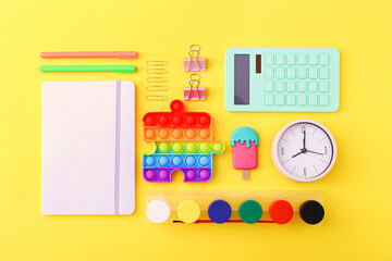 Flat lay of stationery, clock and silicone toys popit on yellow background