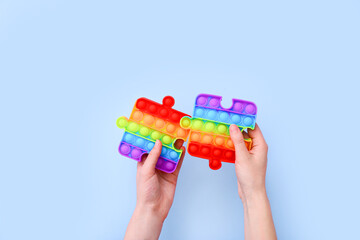 Popit toys in the form of puzzles in hands on a blue background. Multicolored Pop it toy