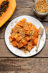 Cutted papaya fruit with granola muesli for breakfast on wooden background