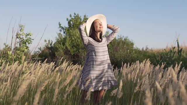 A young woman in a hat and dress in the wind in nature enjoying the sunset.Slow motion