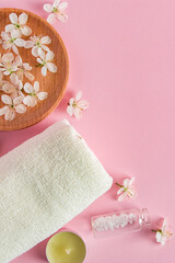 Cosmetic products for spa and aromatherapy. Candles, sea salt, towel and flowers on a pink background. Skin care and beauty concept.