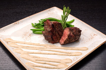Filet mignon with asparagus on a light plate, on a dark background