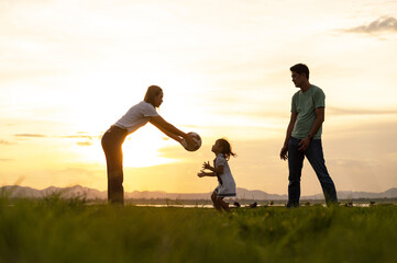 Silhouette Happy Asian family. Father, mother and daughter playing a football outdoors