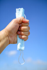 End of quarantine, covid-19. Man holding used medical mask on clear sky background. End of coronavirus pandemic and back to normal life again. Copy space. Coronavirus stop concept, after COVID-19.
