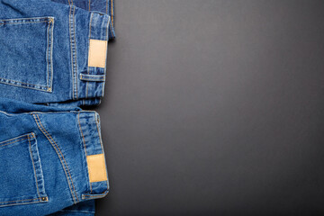 Classic blue jeans. Casual pants clothing blue jeans with brown blank leather labels on black background with copy space. Top view