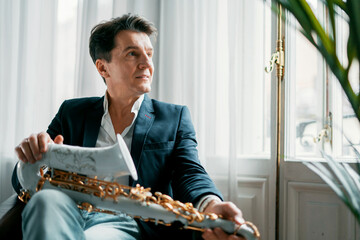 A middle-aged male artist of European appearance in his apartment. Holds a saxophone at home....