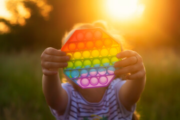 The child plays with a colorful rainbow game of poppit. Silicone fidget close-up.