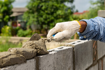 Masonry worker make concrete wall by cement block and plaster at construction site.