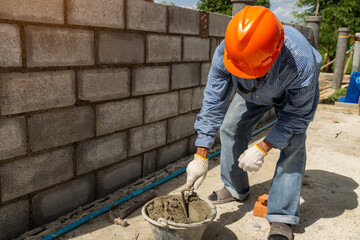 Masonry worker make concrete wall by cement block and plaster at construction site.