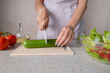 person cutting vegetables
Female hands hold a knife and cut a cucumber for salad making. Cooking salad in the kitchen against the background of a woman in an apron.