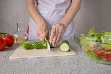 person cutting vegetables
Female hands hold a knife and cut a cucumber for salad making. Cooking salad in the kitchen against the background of a woman in an apron.