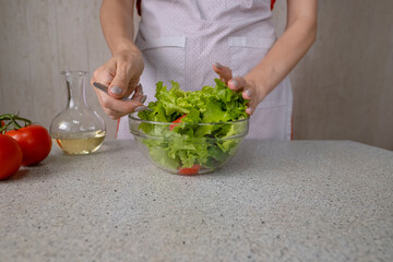 Female hands throw torn lettuce leaves in a dish. Cooking salad in the kitchen on the background of a woman in an apron.