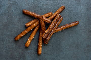 Pretzel rods in a pile on dark gray slate background. 