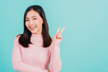 Fototapeta na wymiar Young Asian beautiful woman smiling wear silicone orthodontic retainers on teeth showing v-sign victory finger isolated on blue background, retaining after removable braces. Dental hygiene concept