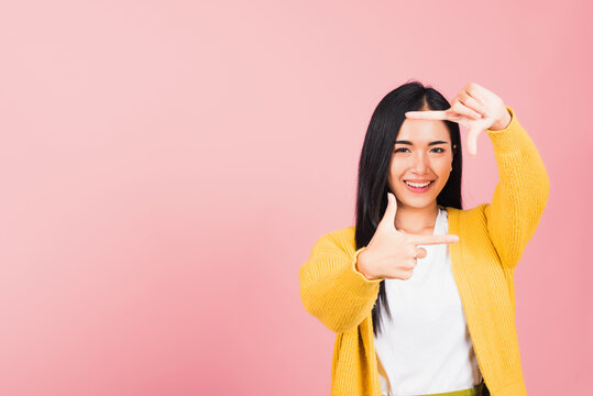 Portrait Asian beautiful happy young woman photographer smile execute finger making frame gesture front face for photography, studio shot isolated on pink background