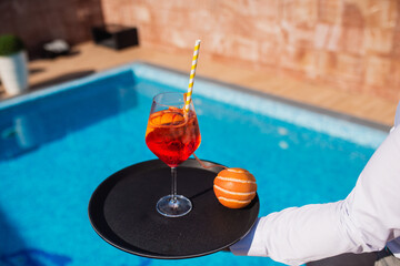 Barman serving cocktail and orange in high end resort by the pool. Summer hot party